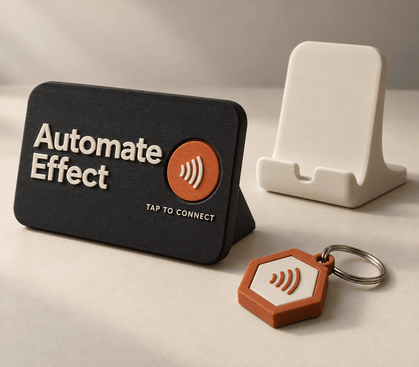 A dark Automate Effect NFC stand with an orange tap symbol, beside a white phone stand and an orange hexagonal NFC keychain